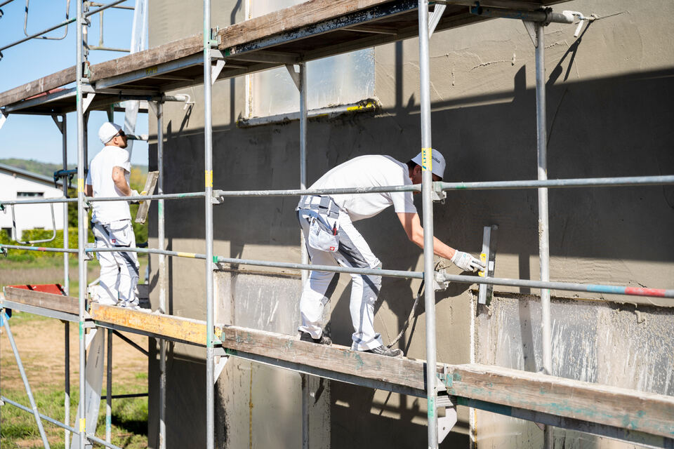 Mitarbeiter verputzt eine Außenwand vom Gerüst aus