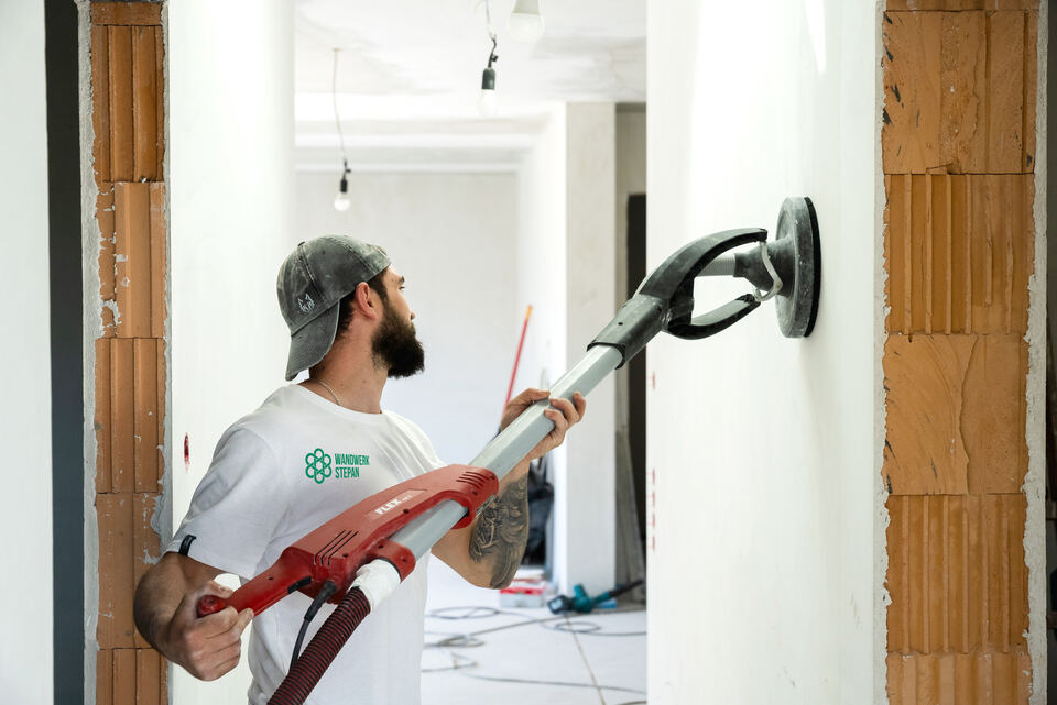 Mitarbeiter schleift eine Wand mit dem Langhalsschleifer