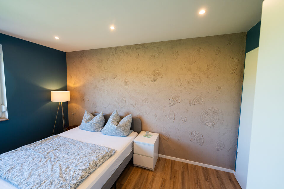 Akzentwand im Muschellook hinter dem Bett, warm beleuchtet